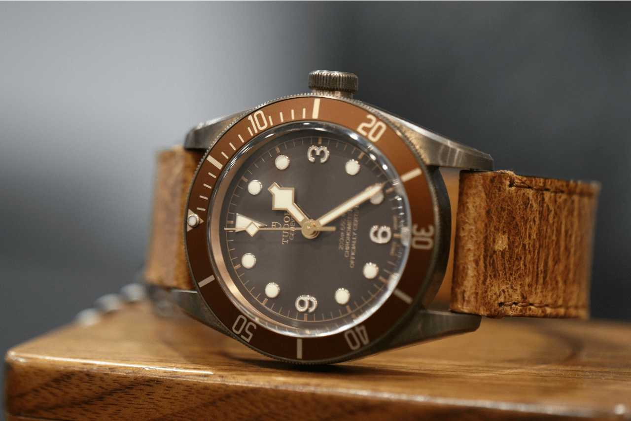 A TUDOR vintage-style wristwatch with a brown leather strap on a wooden surface.