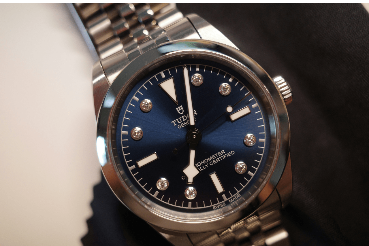 A TUDOR silver luxury watch with a deep blue dial, diamond hour markers, and a metal bracelet.