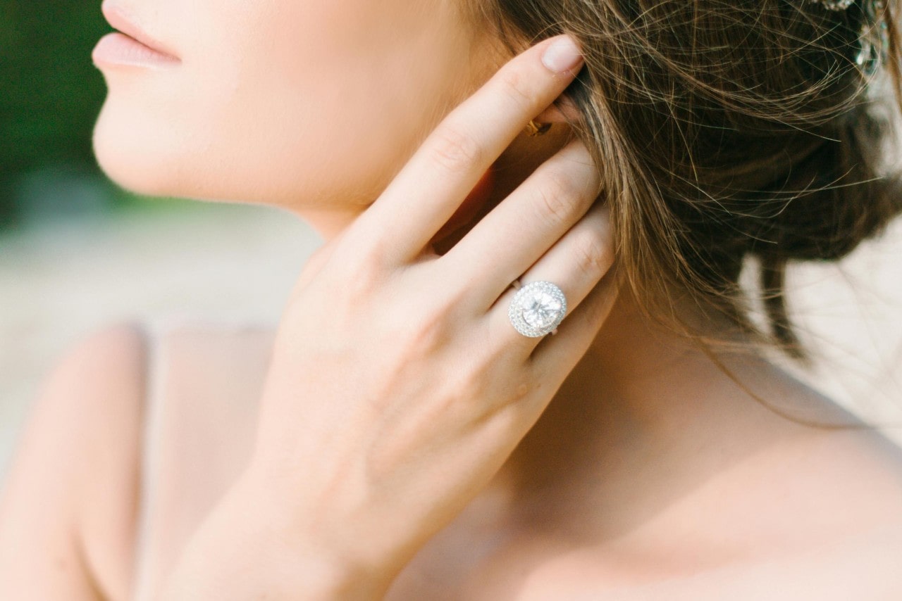 A woman fixes her hair, while showcasing a big halo diamond engagement ring.