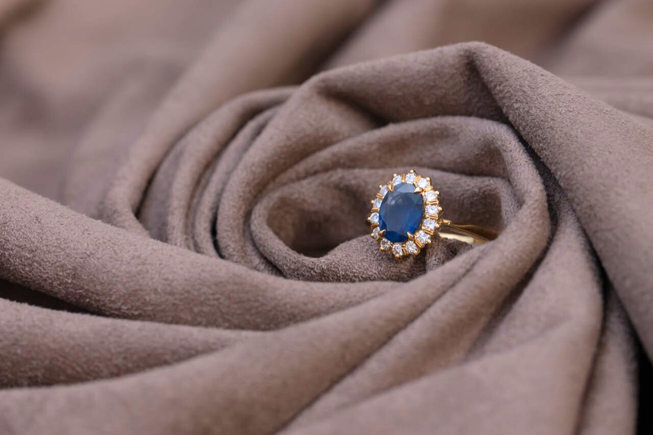 A close-up of a sapphire engagement ring with a diamond halo, wrapped in brown fabric.