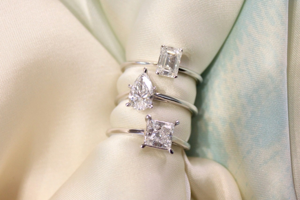 Three different cut engagement rings with a silk fabric stuffed inside them.