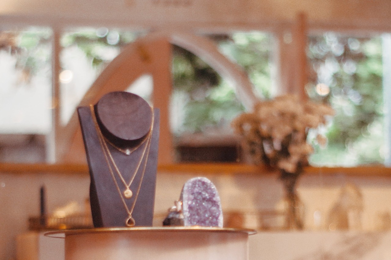 Elegant jewelry display with layered necklaces on a stand and a purple geode on a table.