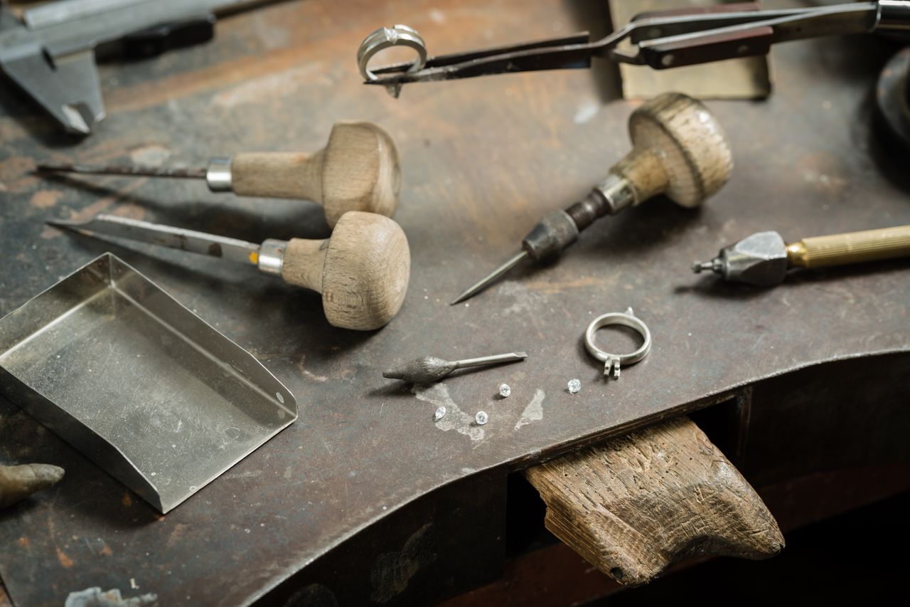 Jewelry-making tools and loose diamonds are arranged on a craftsman&rsquo;s workbench with an unfinished ring.