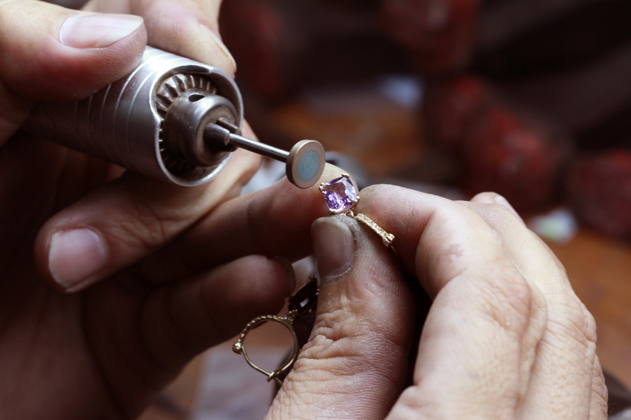 A jeweler polishes a yellow gold gemstone ring setting using a rotary tool.