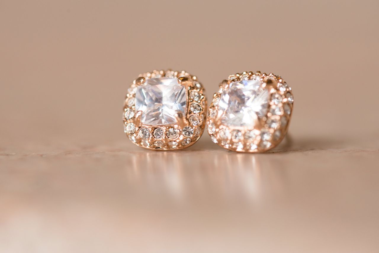 A pair of rose gold earrings with square-cut gemstones and intricate detailing sparkle on a neutral surface.