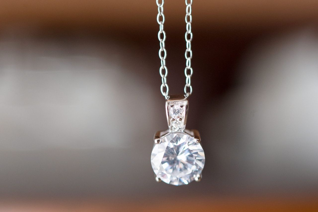 A silver necklace with a brilliant round-cut pendant dangles from a chain.