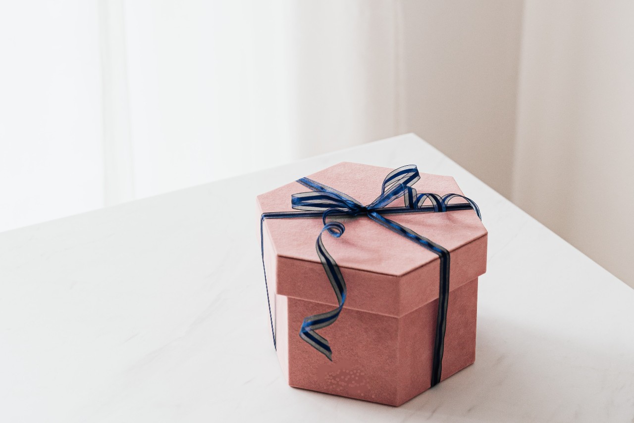 A pink hexagonal gift box adorned with a blue ribbon sits on a white marble surface