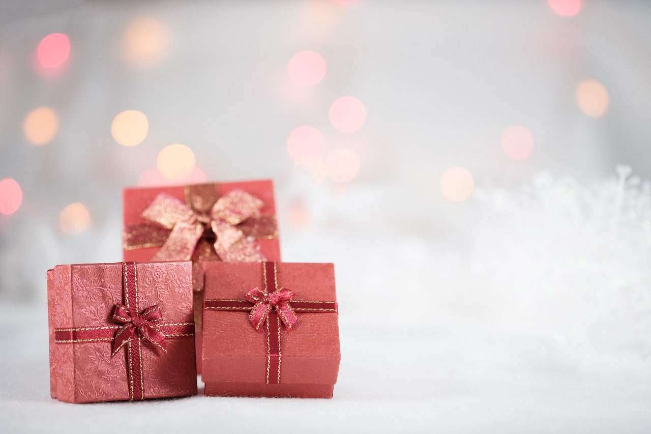 Three small red gift boxes with gold ribbons are set against a blurred background of warm, glowing lights.