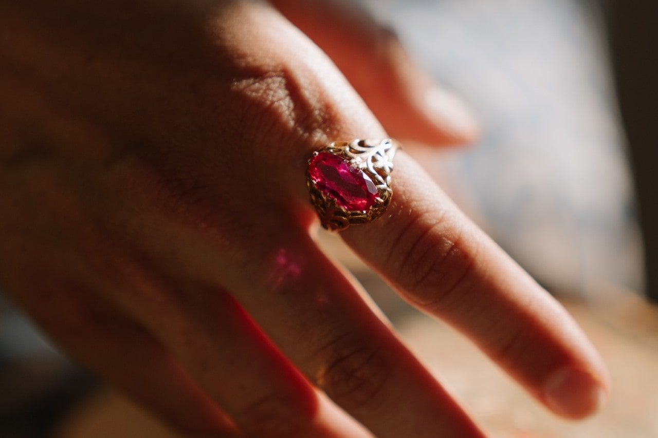 an outstretched hand wearing an elaborate cocktail ring with a ruby center stone.