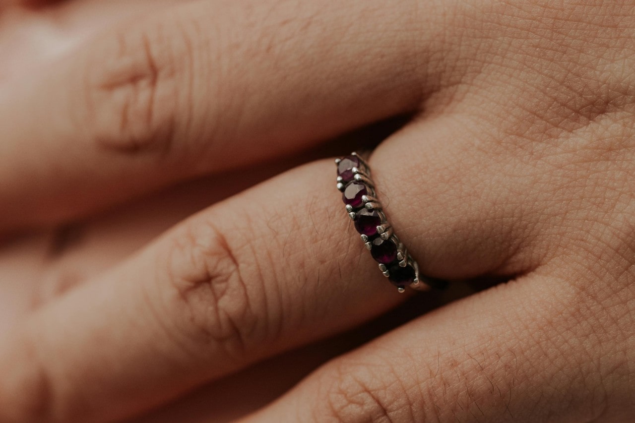 A silver wedding band set with a row of dark red rubies on a hand.