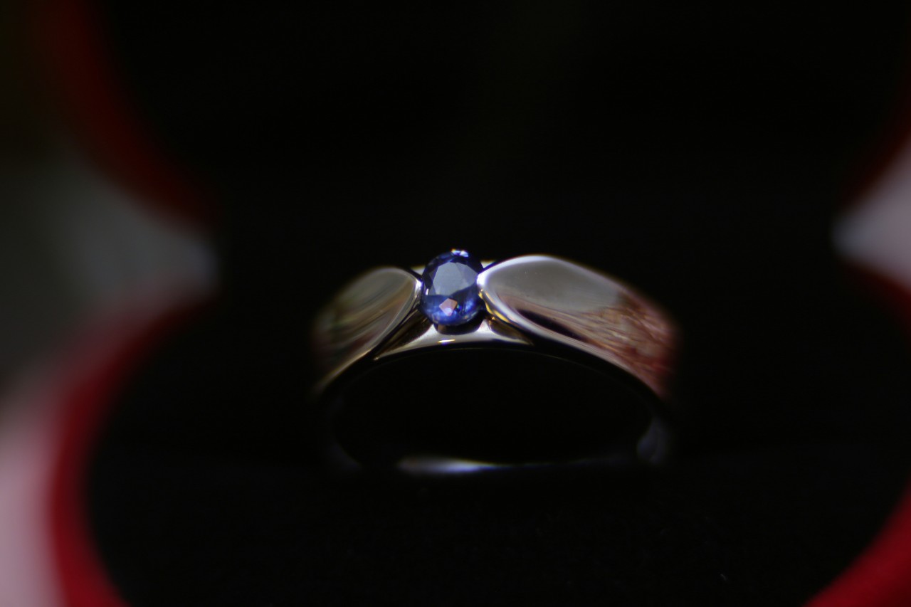 A polished white gold ring with a single blue sapphire centre stone displayed in a black and red velvet ring box.