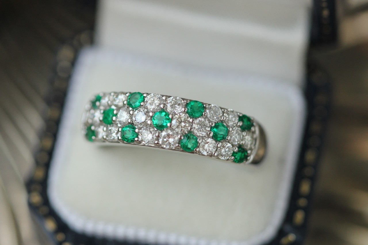 A close up of a round-cut emerald and diamond three raw wedding band inside the white jewelry box.