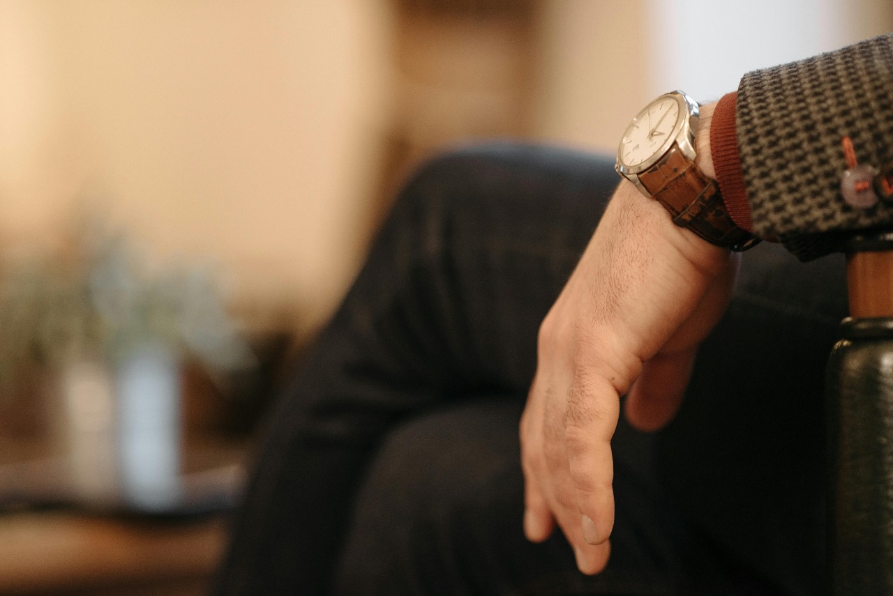 A close-up of a man’s hand resting on the arm of a chair, wearing a silver watch with brown leather strap