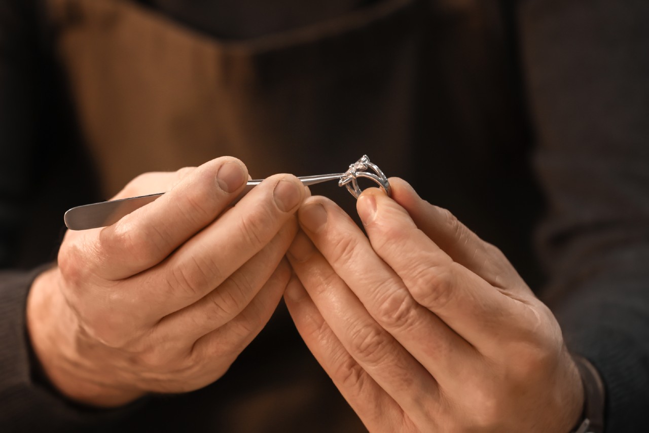 Close-up of a jeweler’s hands adjusting a diamond ring with tweezers.