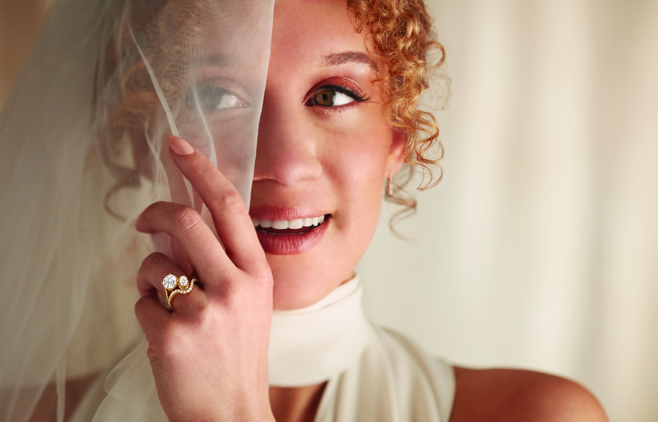 bride peeking out from her veil and showing off her moi et toi engagement ring with nesting wedding band