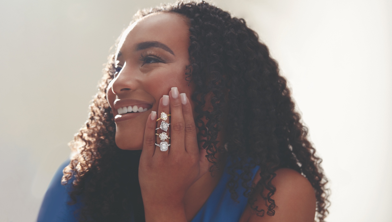 Four halo engagement rings on the finger of a smiling woman.