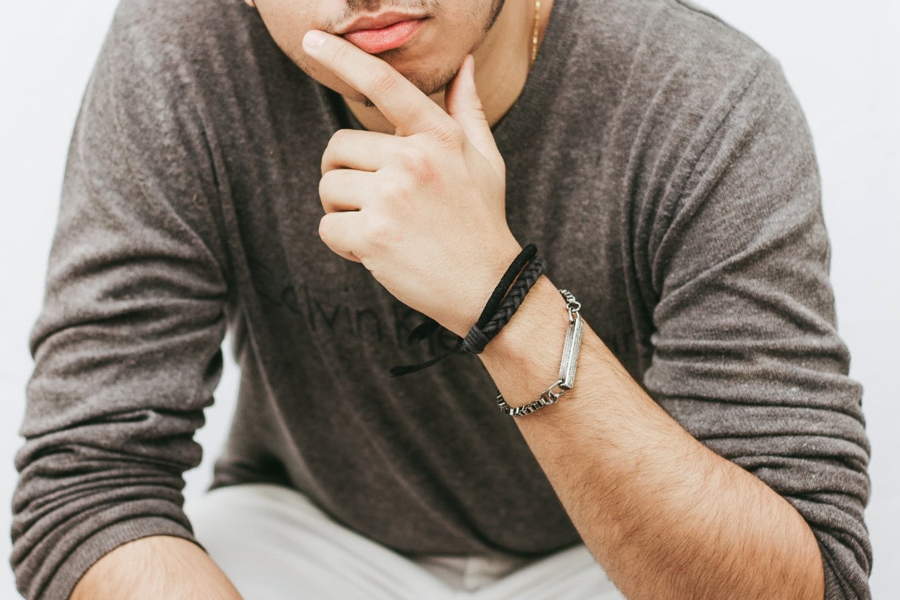 A close up of a man in a grey sweater with rubber and steel bracelets.