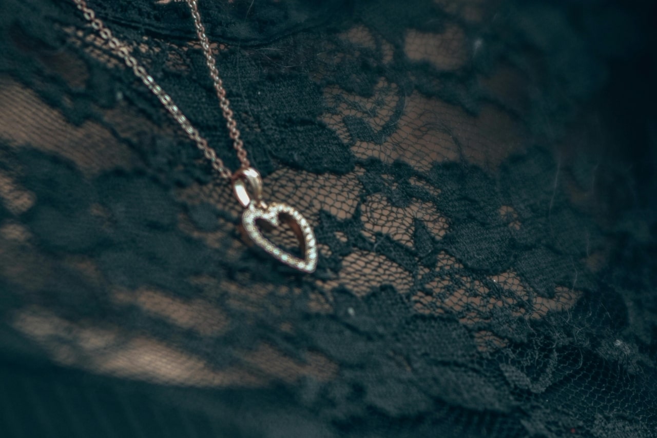 A close-up of a person wearing a diamond open-heart pendant necklace over a black lace blouse.
