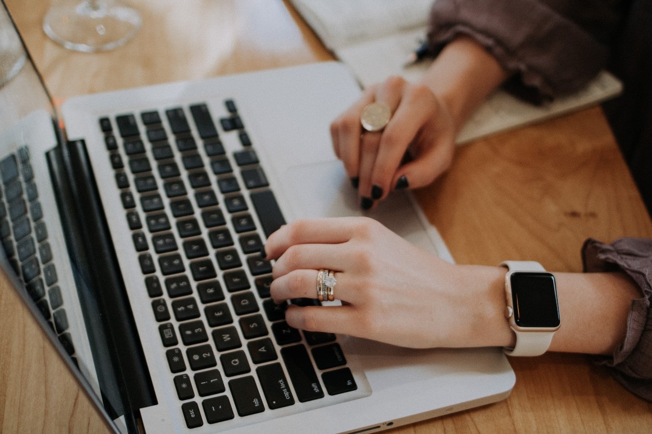 A woman typing on a computer while wearing a smartwatch and wedding ring set.