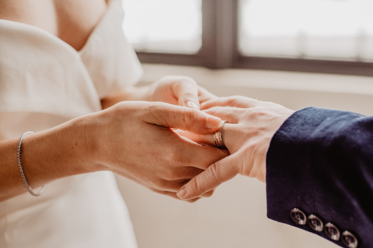 A bride placing a wedding ring on the groom’s finger during a wedding ceremony.