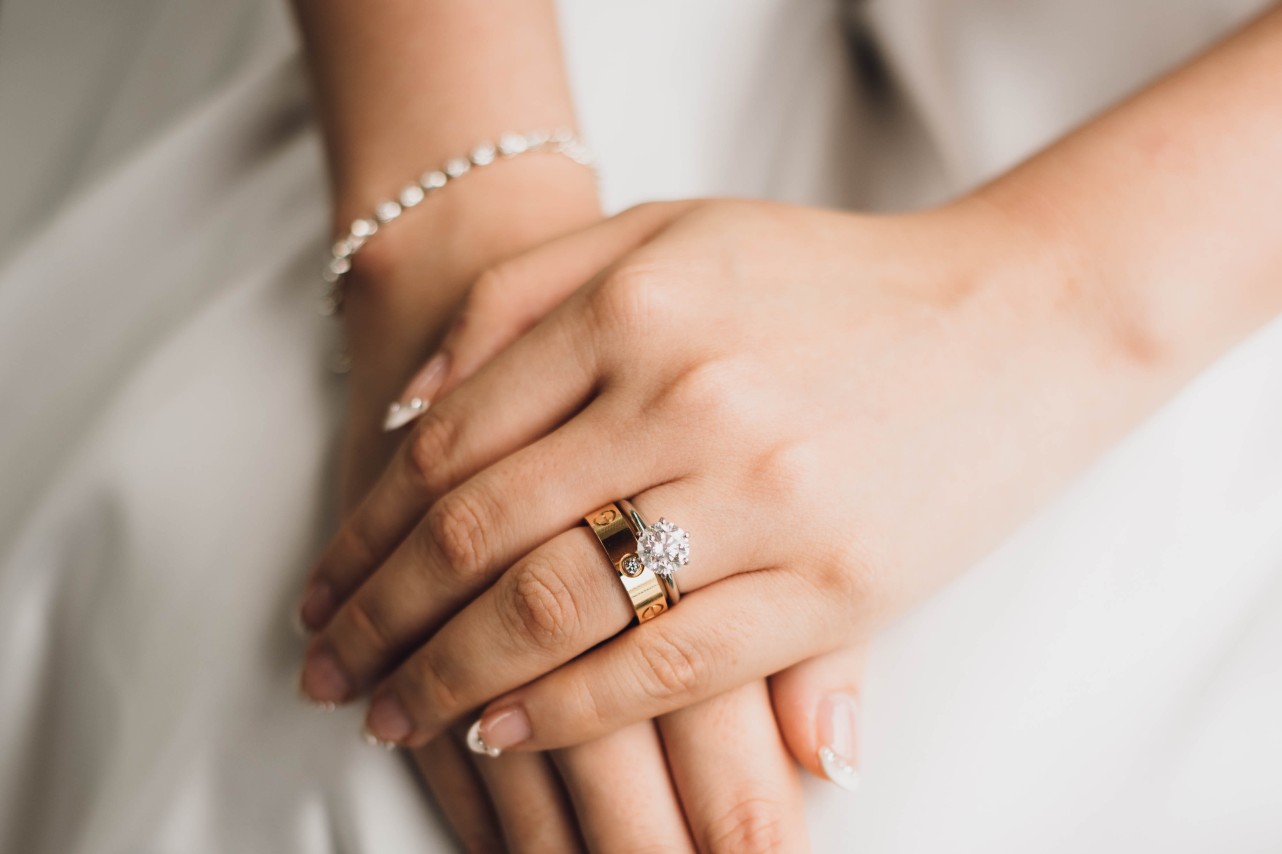 A close up of a bride’s hands, showcasing solitaire diamond engagement ring and yellow gold wedding band.