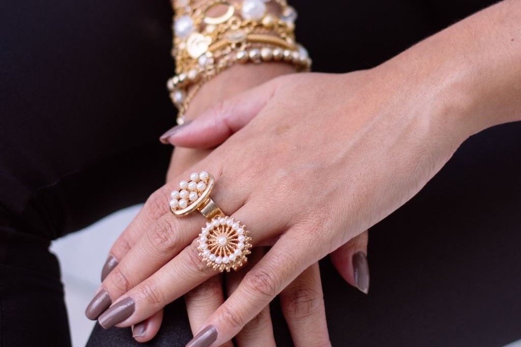 A woman crossing her hands over one another, adorned with yellow gold rings with pearl details.