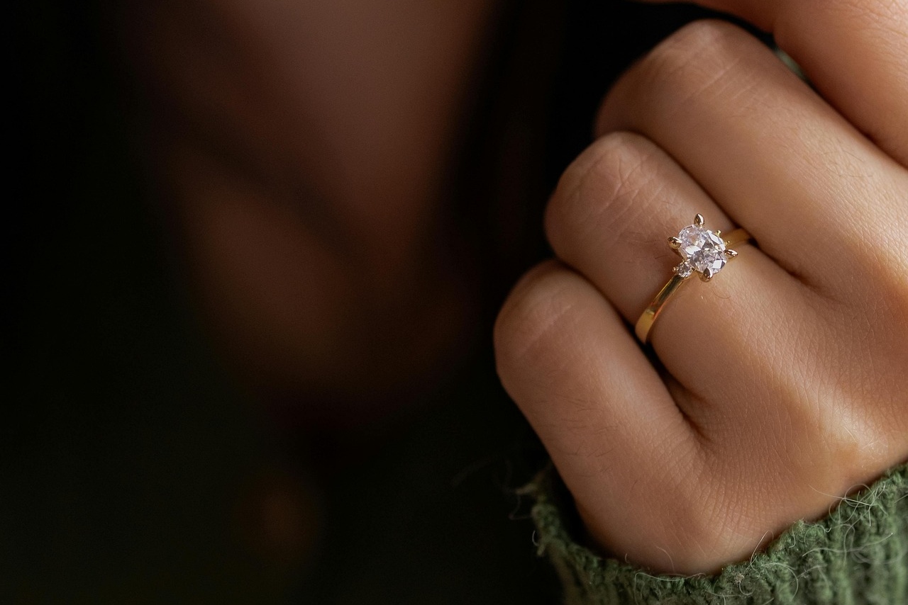 An oval center stone with two small round diamonds flanking the sides on a yellow gold thin band on a woman’s hand
