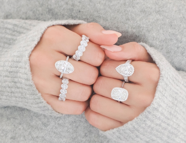 A woman wearing three diamond halo engagement rings and two eternity diamond wedding bands, with three of the rings on one hand and the last two on her other hand.