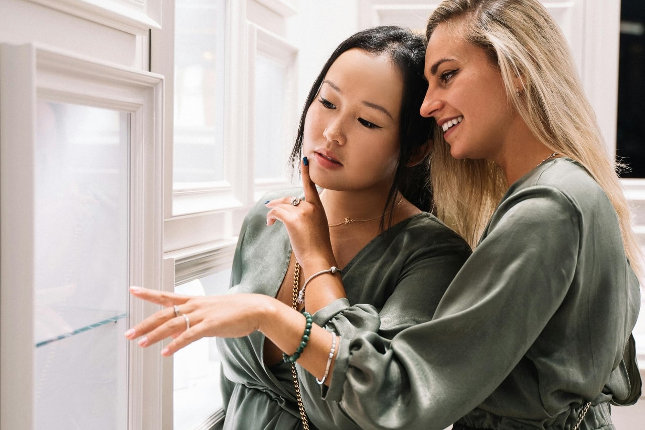 Two women in green tops look intently at jewelry in a display case.