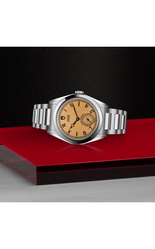 A stainless steel watch with a tan dial, displayed on a glossy red surface against a textured black background.