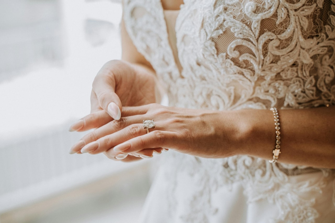 A bride in a lace wedding band showcasing an oval cut diamond engagement ring