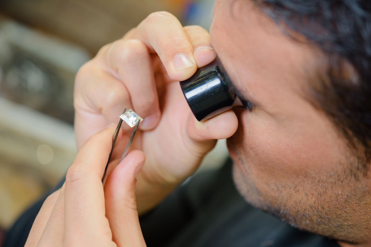 a man looking closely at a princess cut diamond through a magnifying glass