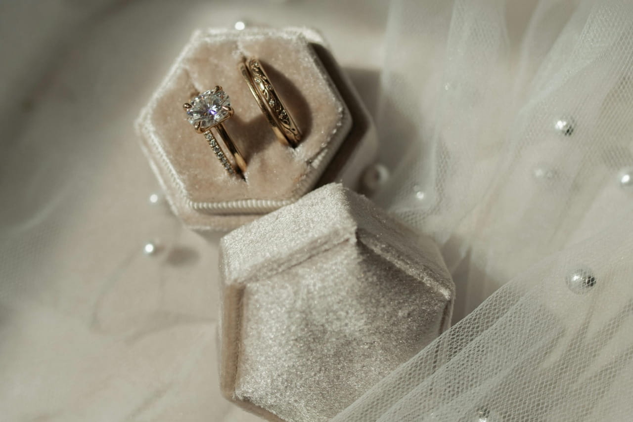 A cream velvet ring box with different wedding bands and engagement rings, sat atop tulle fabric with pearls.