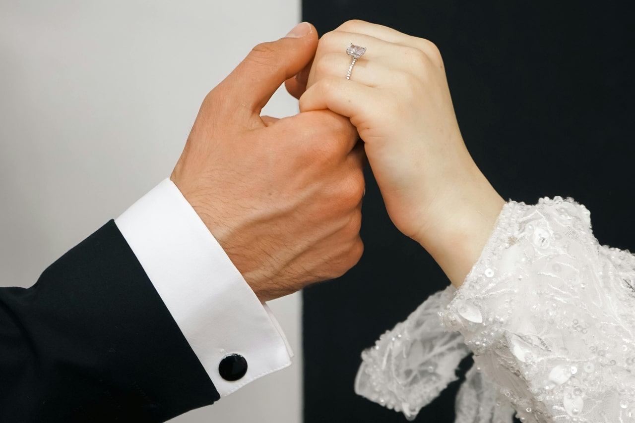 A bride resting her hand in her grooms, showcasing her side-stone engagement ring.