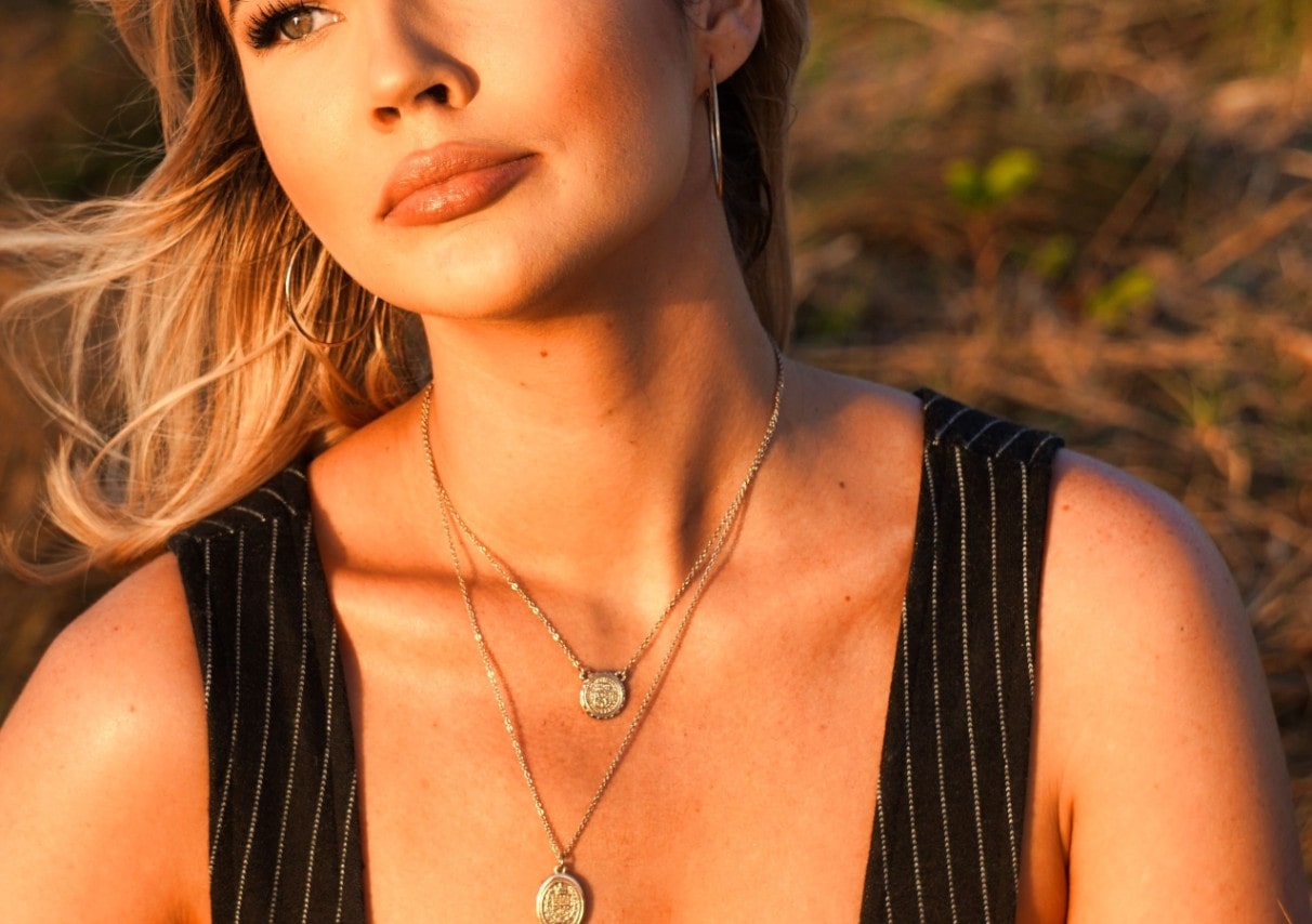 Woman watching the sunset wearing yellow gold necklaces and earrings.