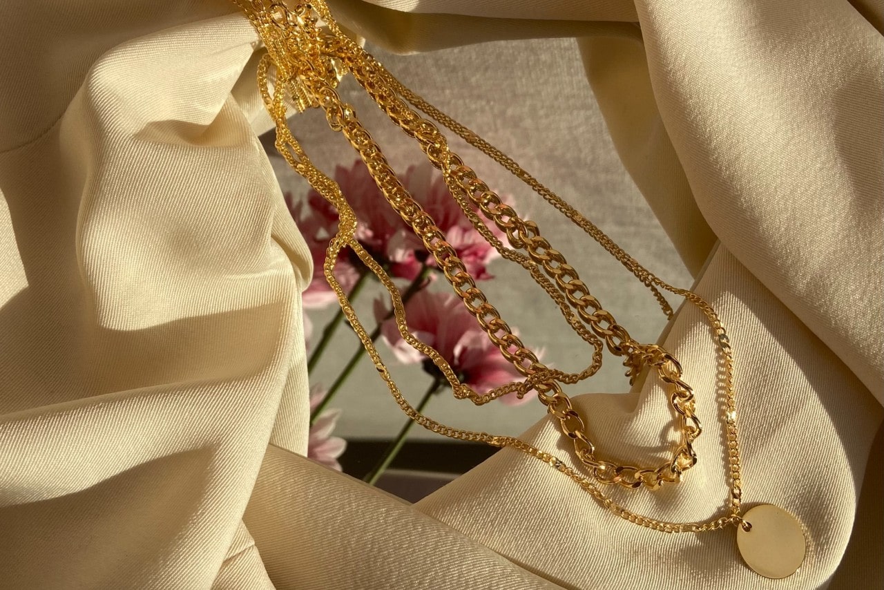 gold necklaces laying across a mirror with flowers reflecting in the center