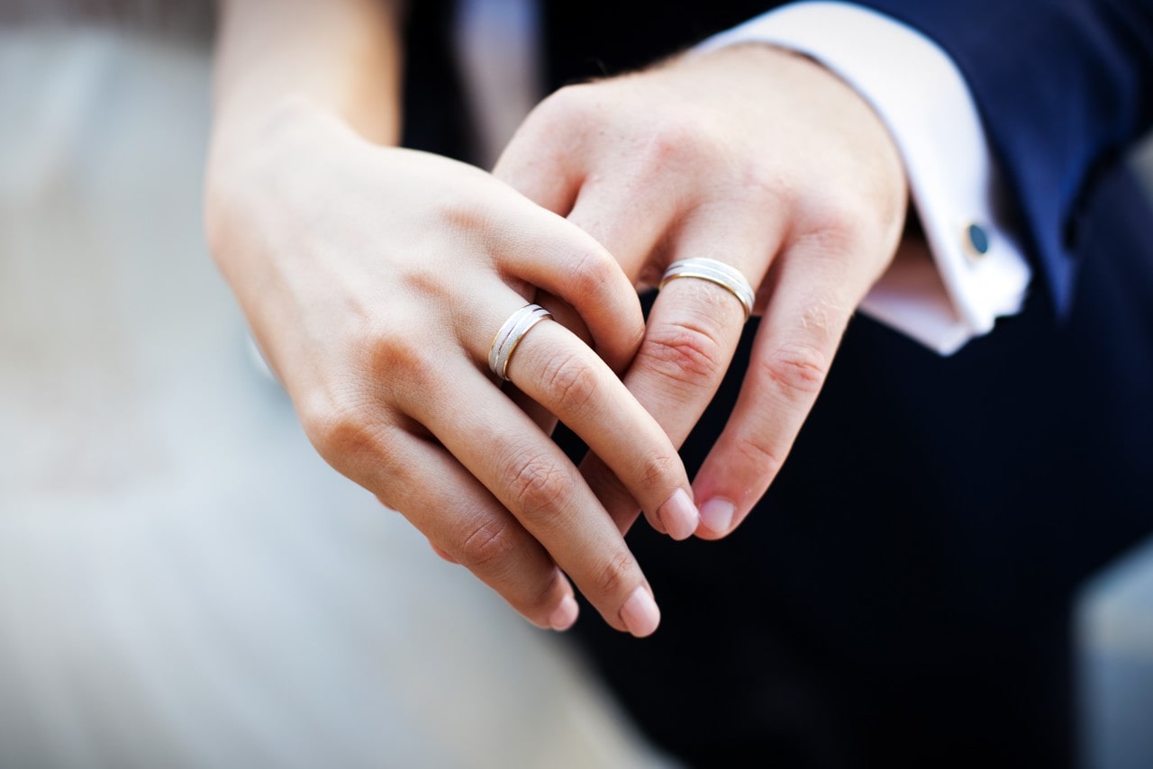A pair of intertwined hands of groom and bride, wearing matching mixed metal wedding bands.