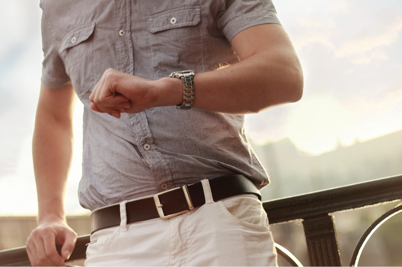 A man in a gray shirt and white trousers checks time with his stainless steel watch.