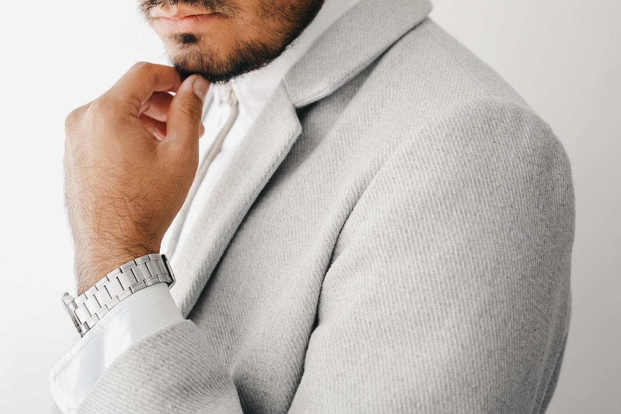 A man in a gray suit puts his hands on his chin, showcasing a stainless steel watch.