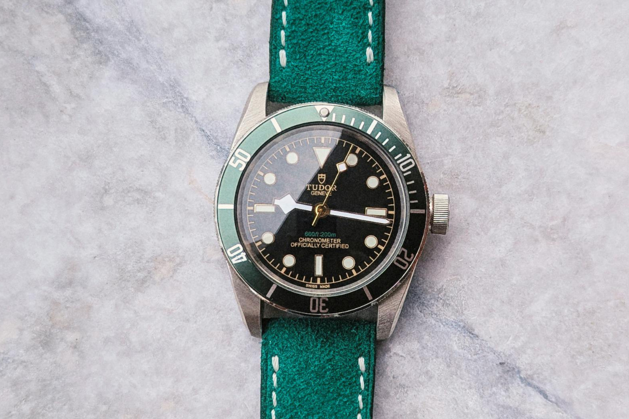 A TUDOR watch with green straps and black dial on a marble surface.