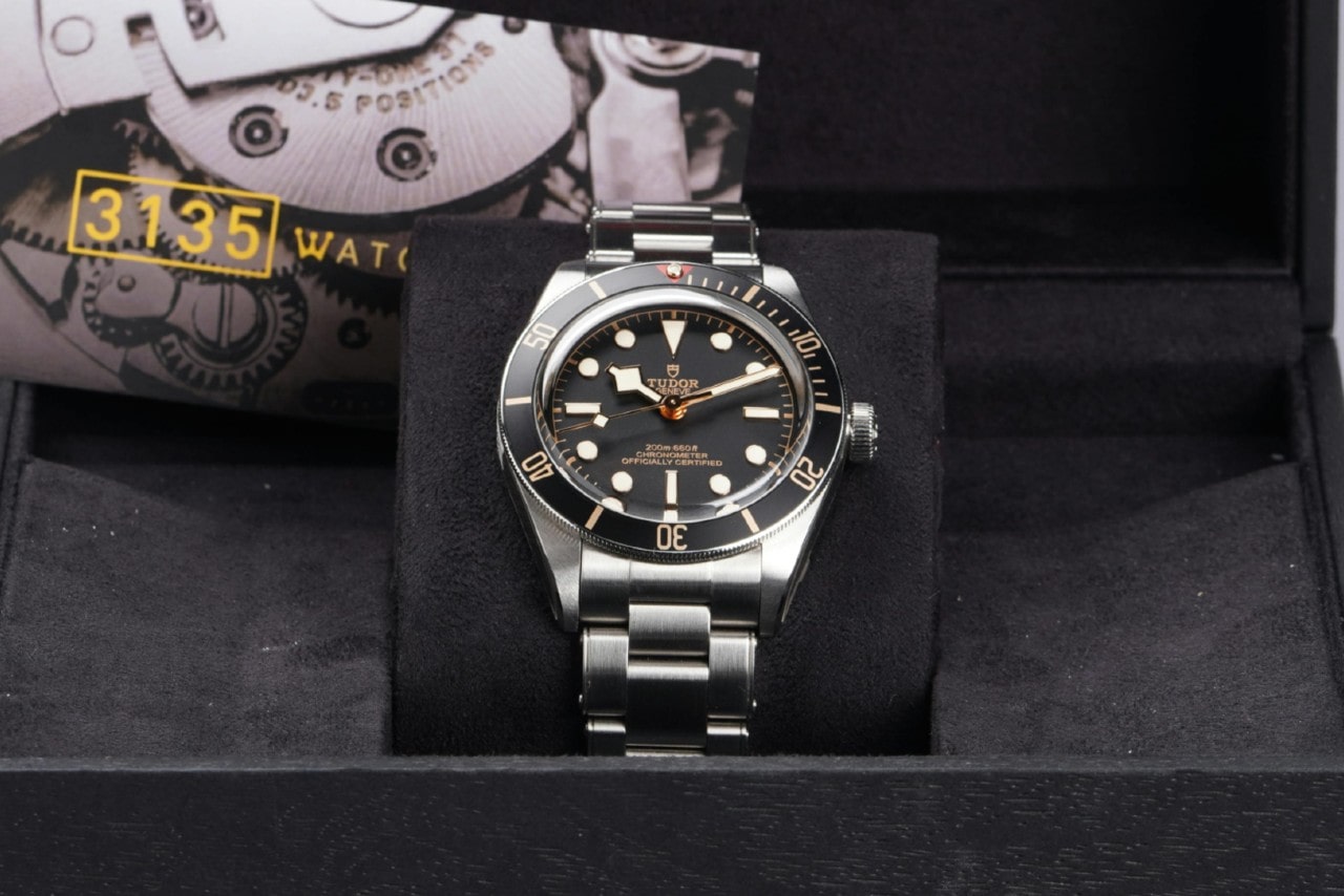 A close-up of a TUDOR stainless steel watch with black dials inside a black box.