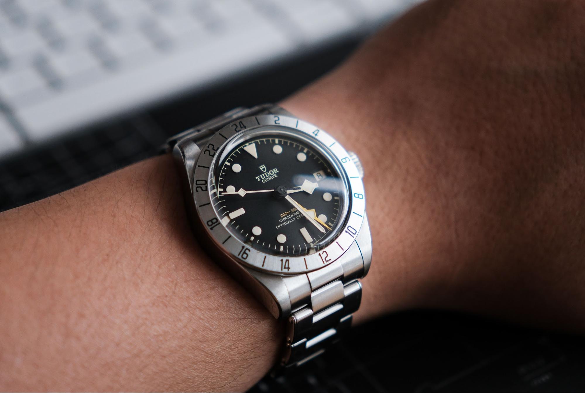Close-up wrist shot of a stainless steel TUDOR watch with a black dial and steel rivet-style bracelet.