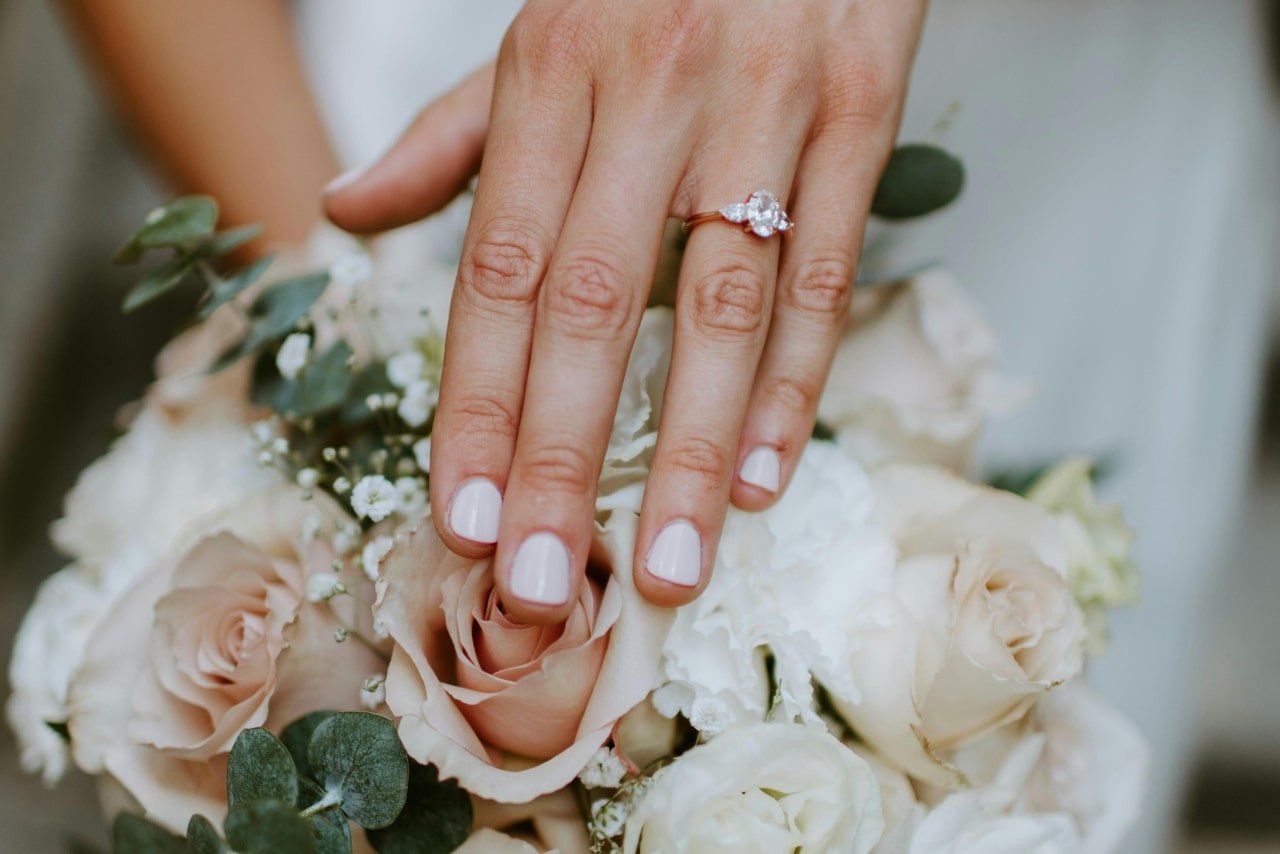 A three stone rose gold diamond engagement ring on a woman&rsquo;s held above the bouquet