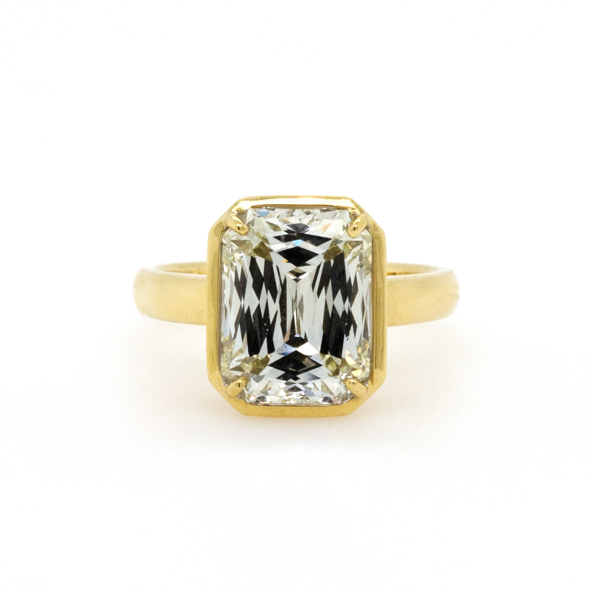 A yellow gold engagement ring with a bezel set emerald cut center stone.