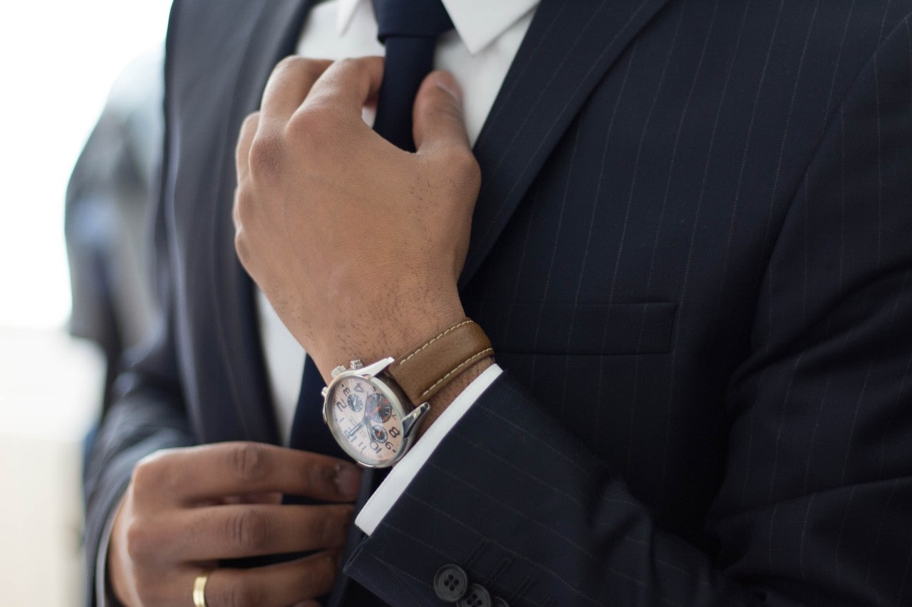 A handsome, fashionable guy (probably a father) sorting out his tie whilst wearing a fine watch.