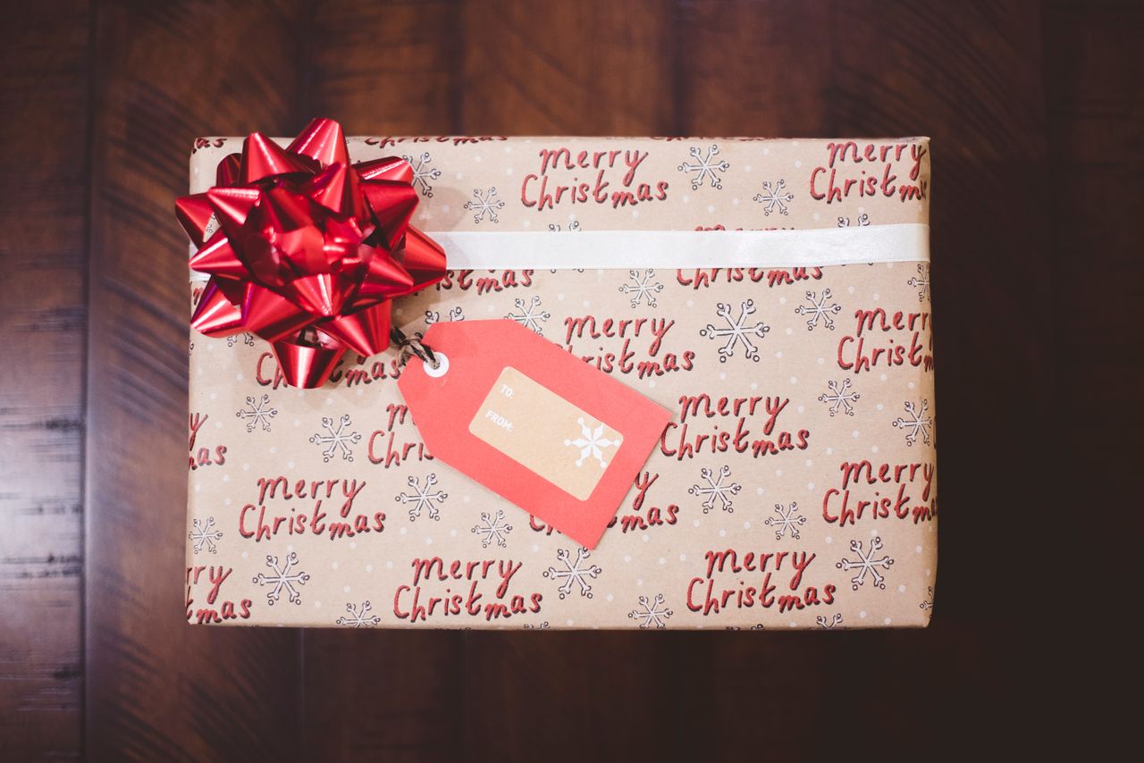 A wrapped Christmas gift with "Merry Christmas" paper, featuring a large red bow and a tag.