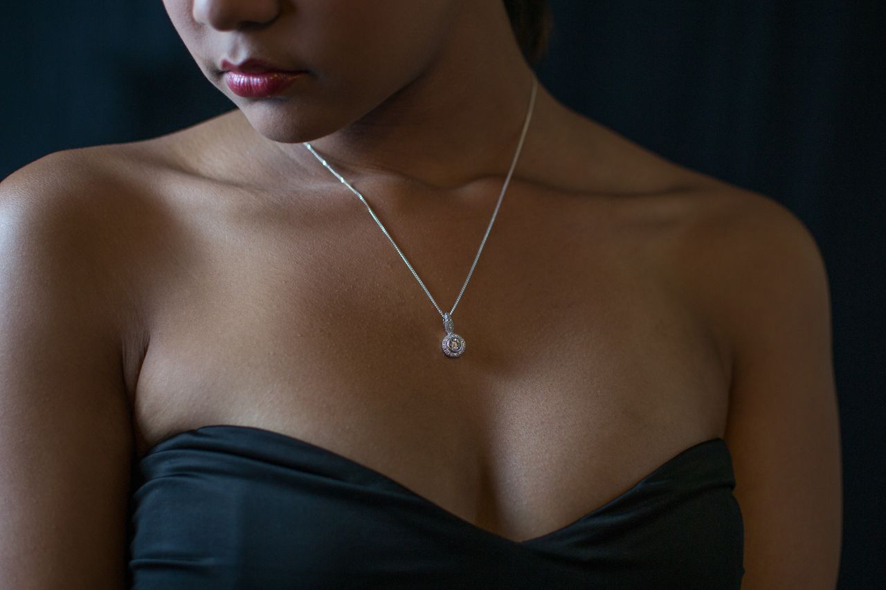 A woman wearing a strapless black dress displays a white gold halo diamond pendant necklace.