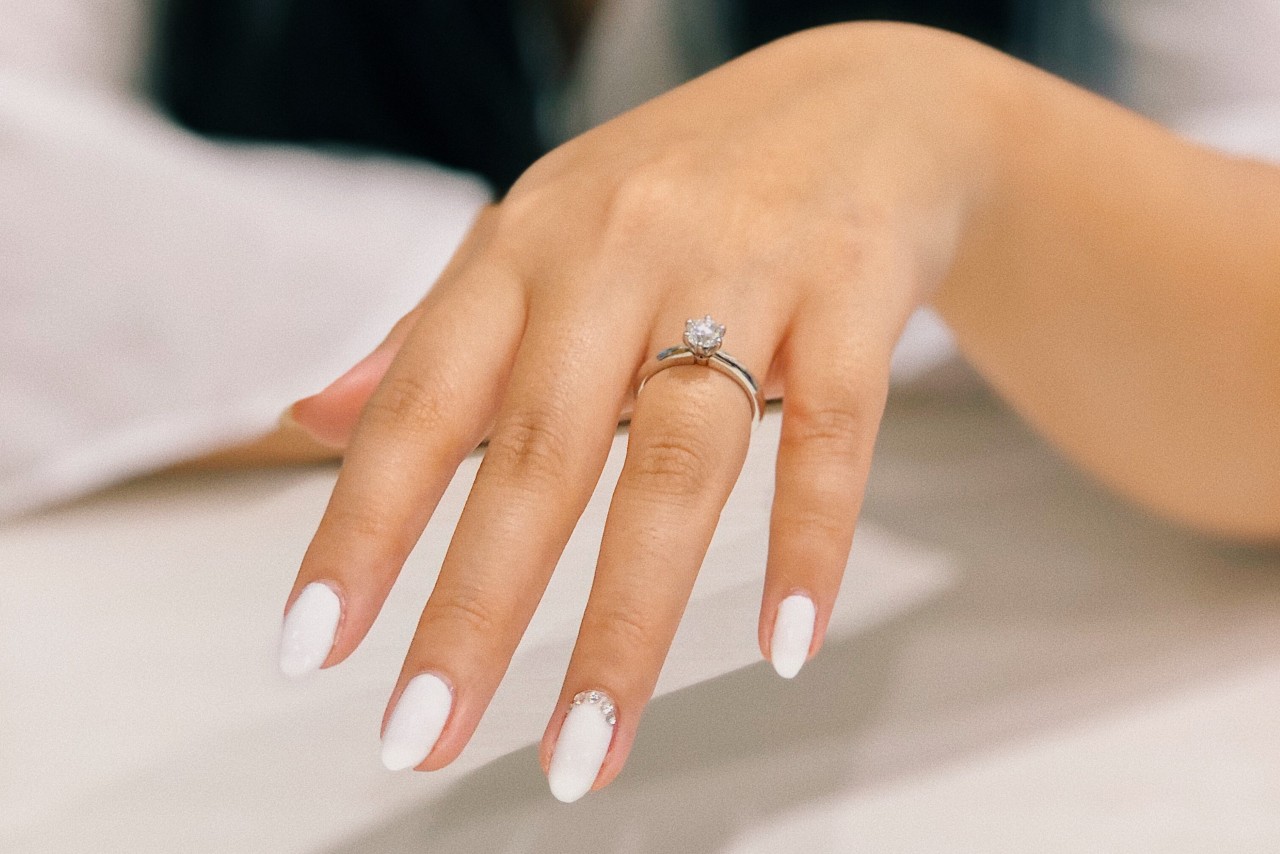 A close-up of a hand with white manicure showcases a platinum classic solitaire diamond engagement ring.