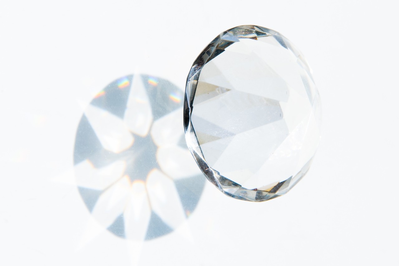 A round brilliant-cut diamond casts a shadow pattern on a white surface.