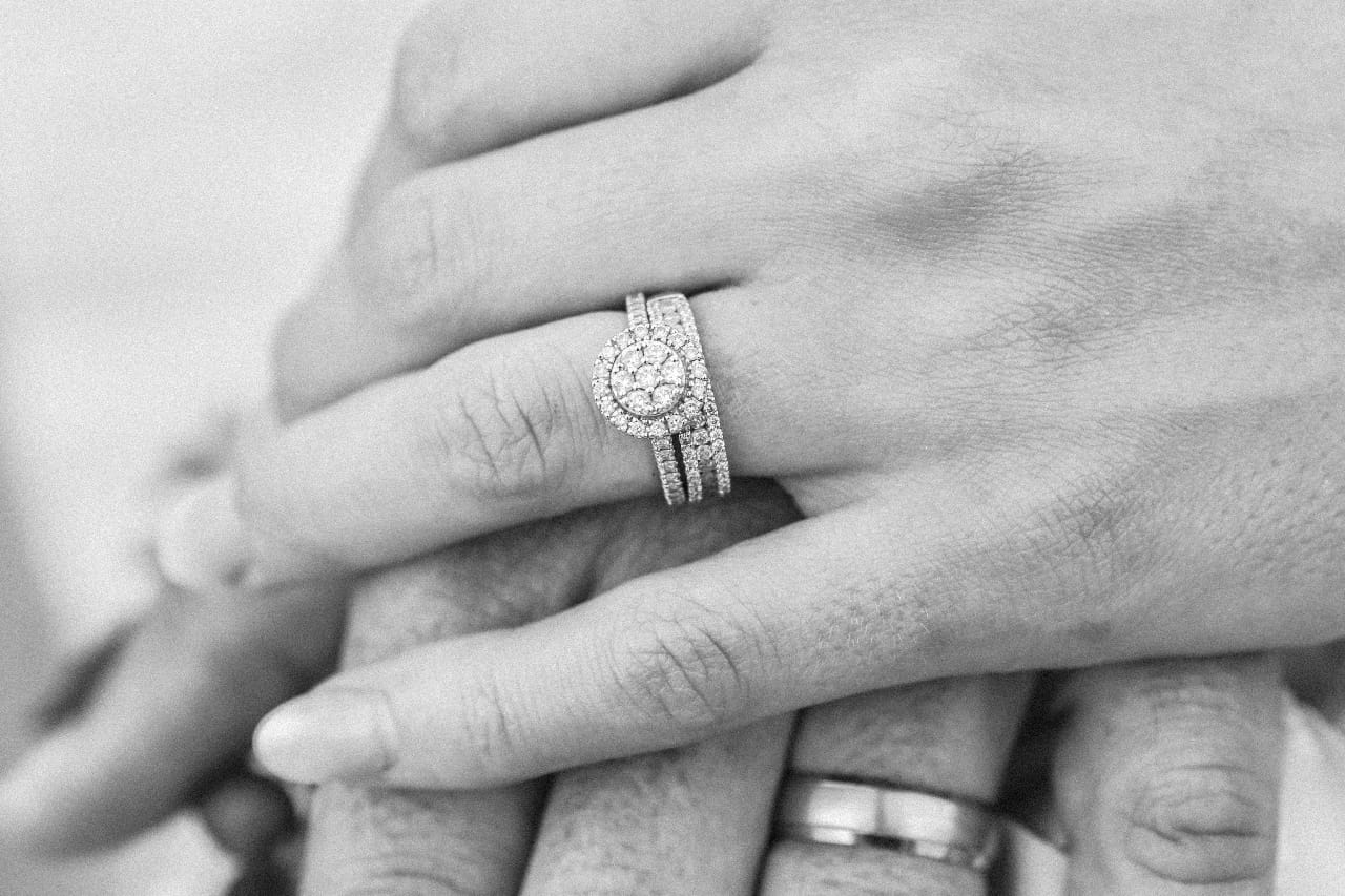 A couple resting their hands together, with a focus on his wedding band and her engagement ring, wedding band, and anniversary band bridal stack.